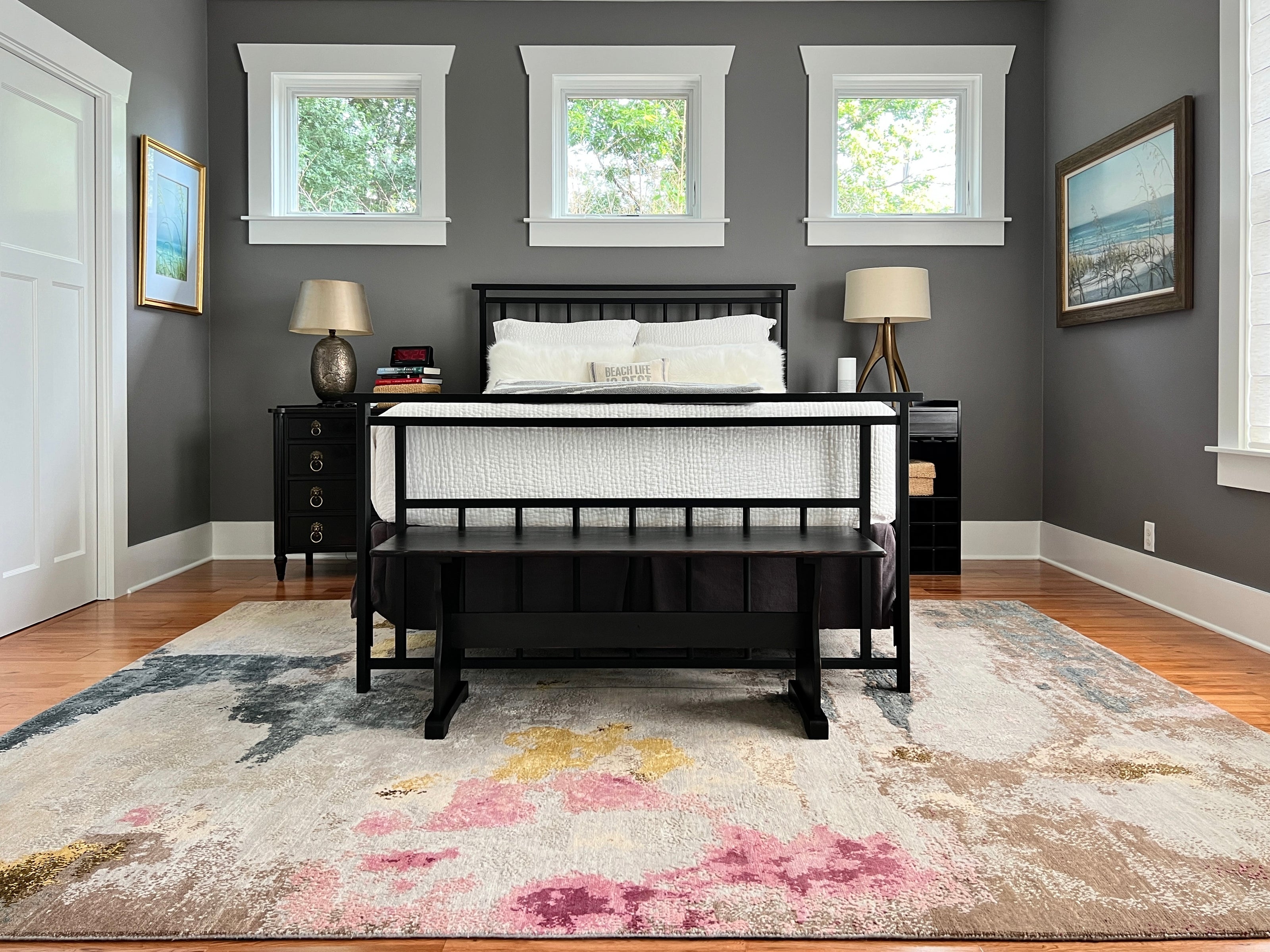 A modern abstract area rug with pink, gold, and grey accents from a Wooden Looms project in Austin, placed under a black bed in a stylish bedroom.