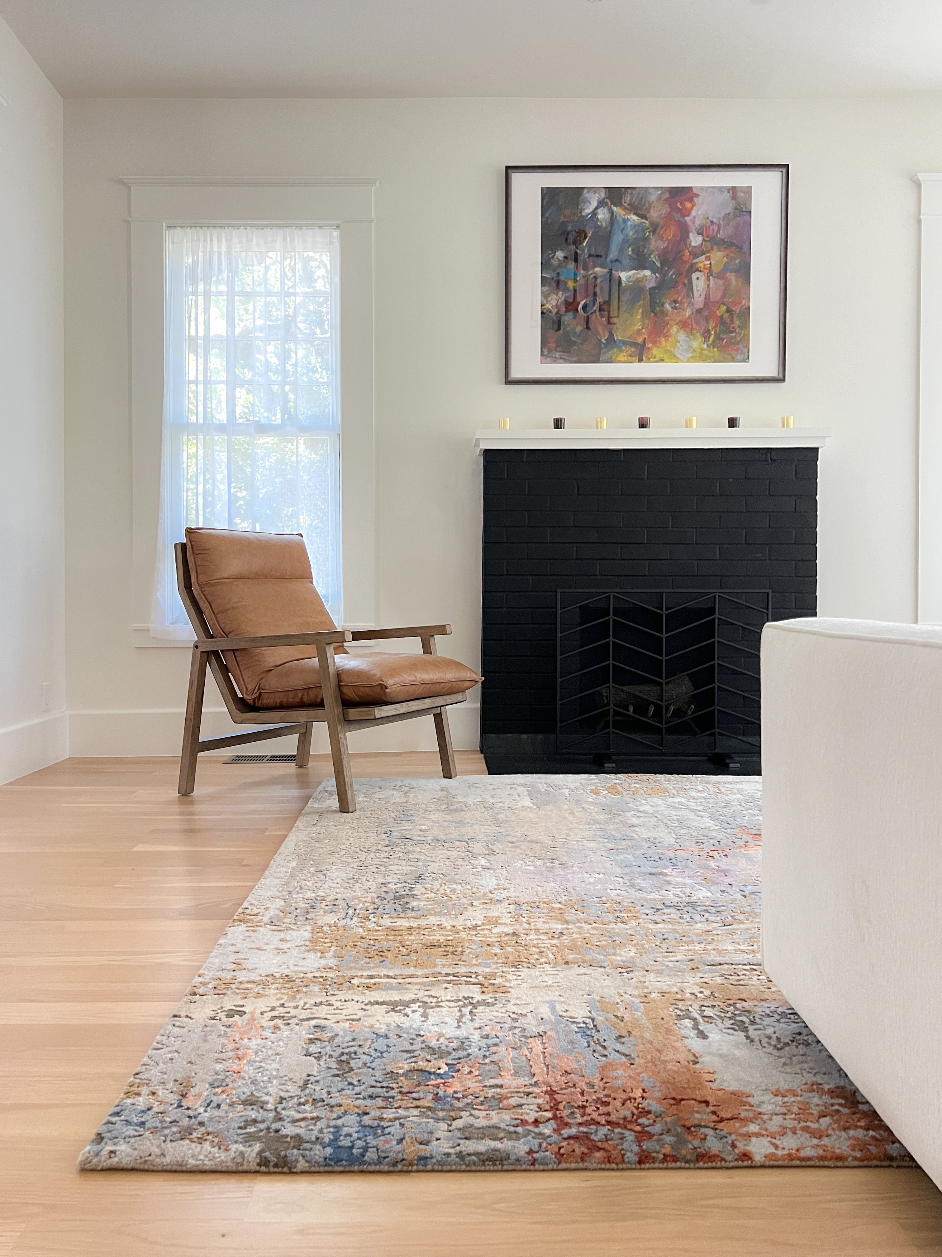 A modern abstract area rug with blue and rust tones, shown in a bright living room project by Wooden Looms in Austin, placed in front of a black brick fireplace.