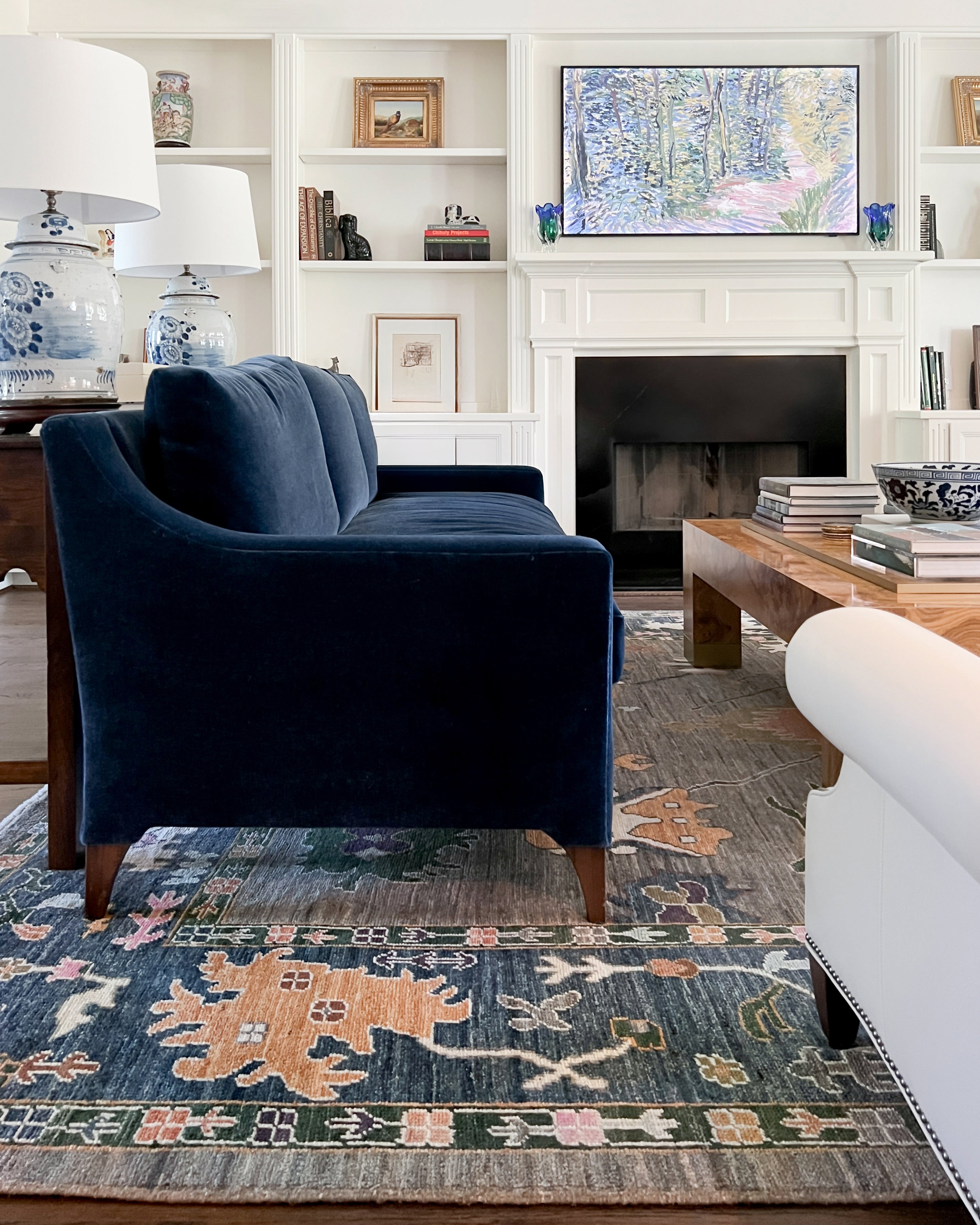 A blue and camel oushak area rug from a Wooden Looms project in Austin, shown in an elegant living room with a navy velvet sofa and built-in shelves.