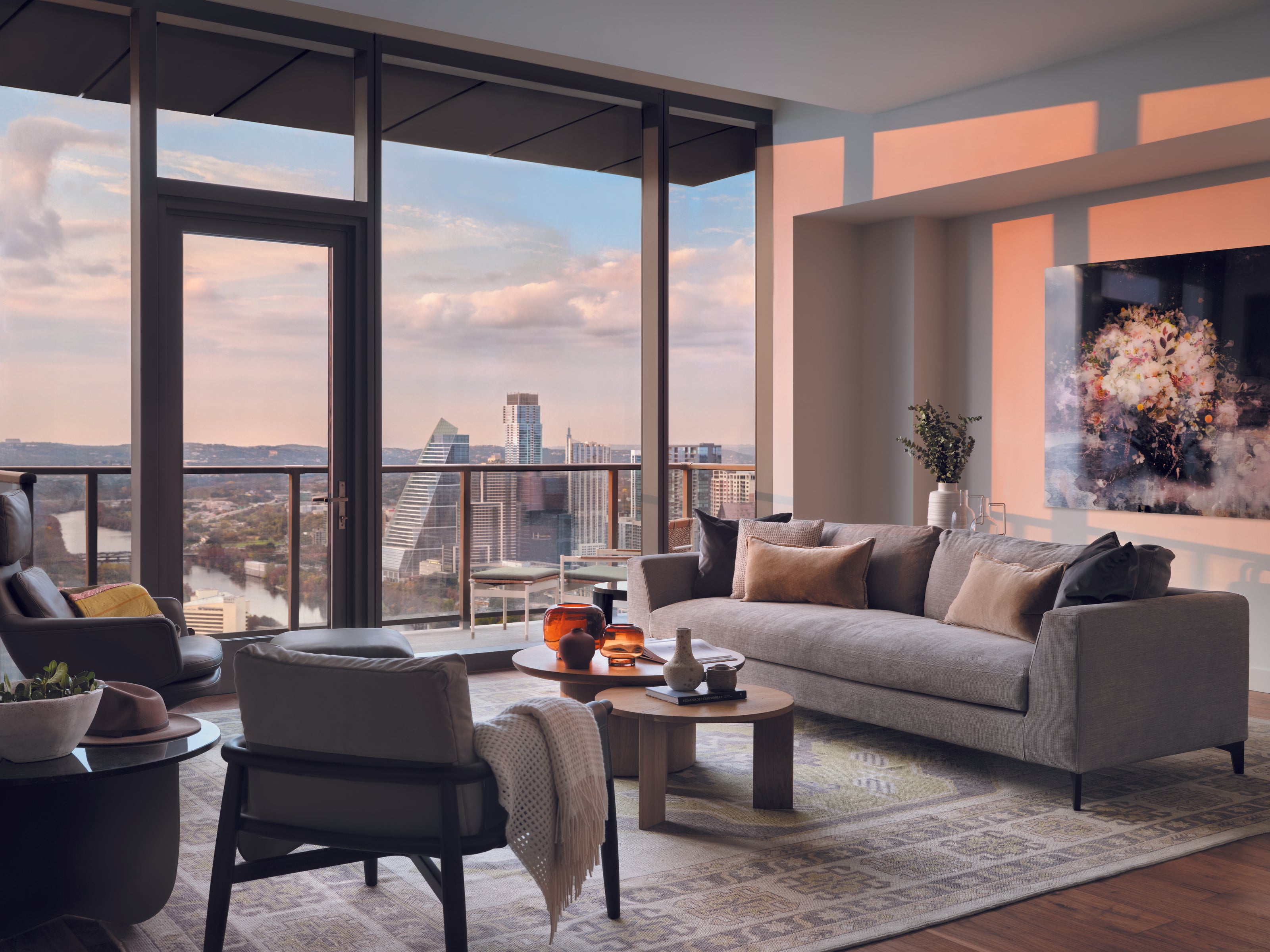 A large turkish oushak area rug with a geometric pattern, featured in a Wooden Looms project in a luxury downtown Austin high-rise apartment with a skyline view at sunset.