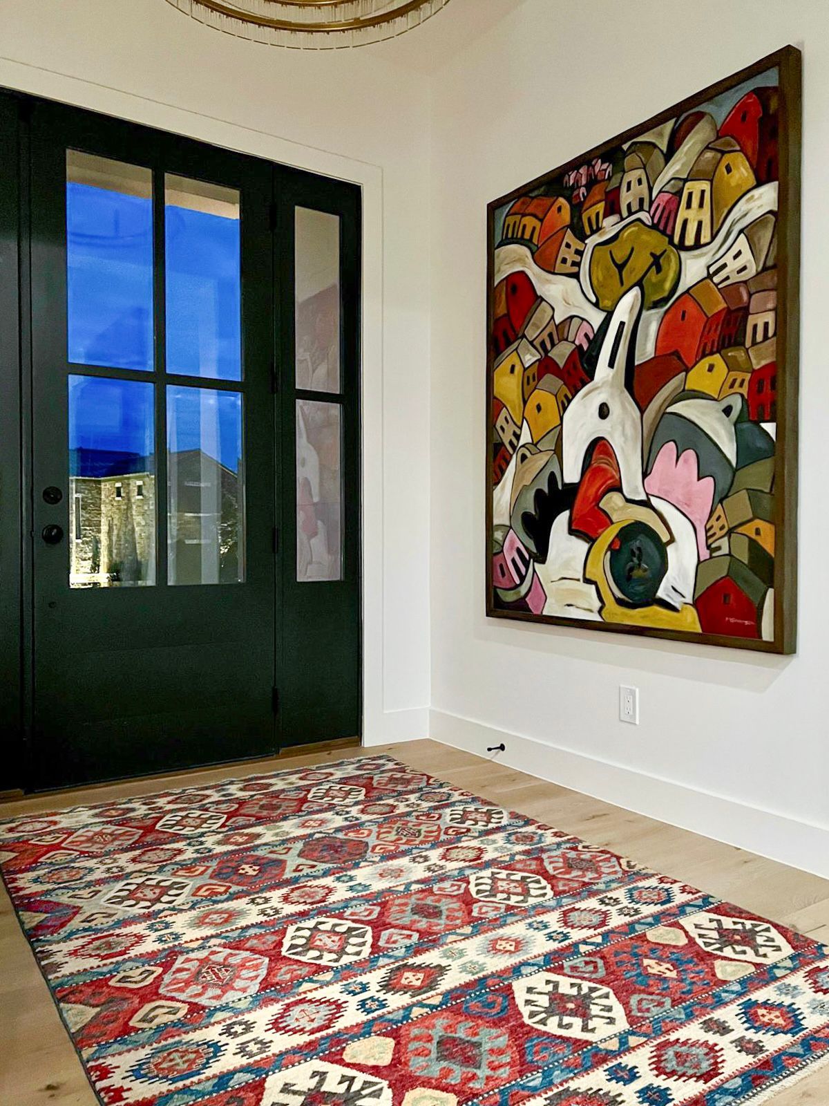 A colorful red and blue tribal rug, featured in a Wooden Looms project in an artistic Austin, TX entryway with a large modern painting on the wall.