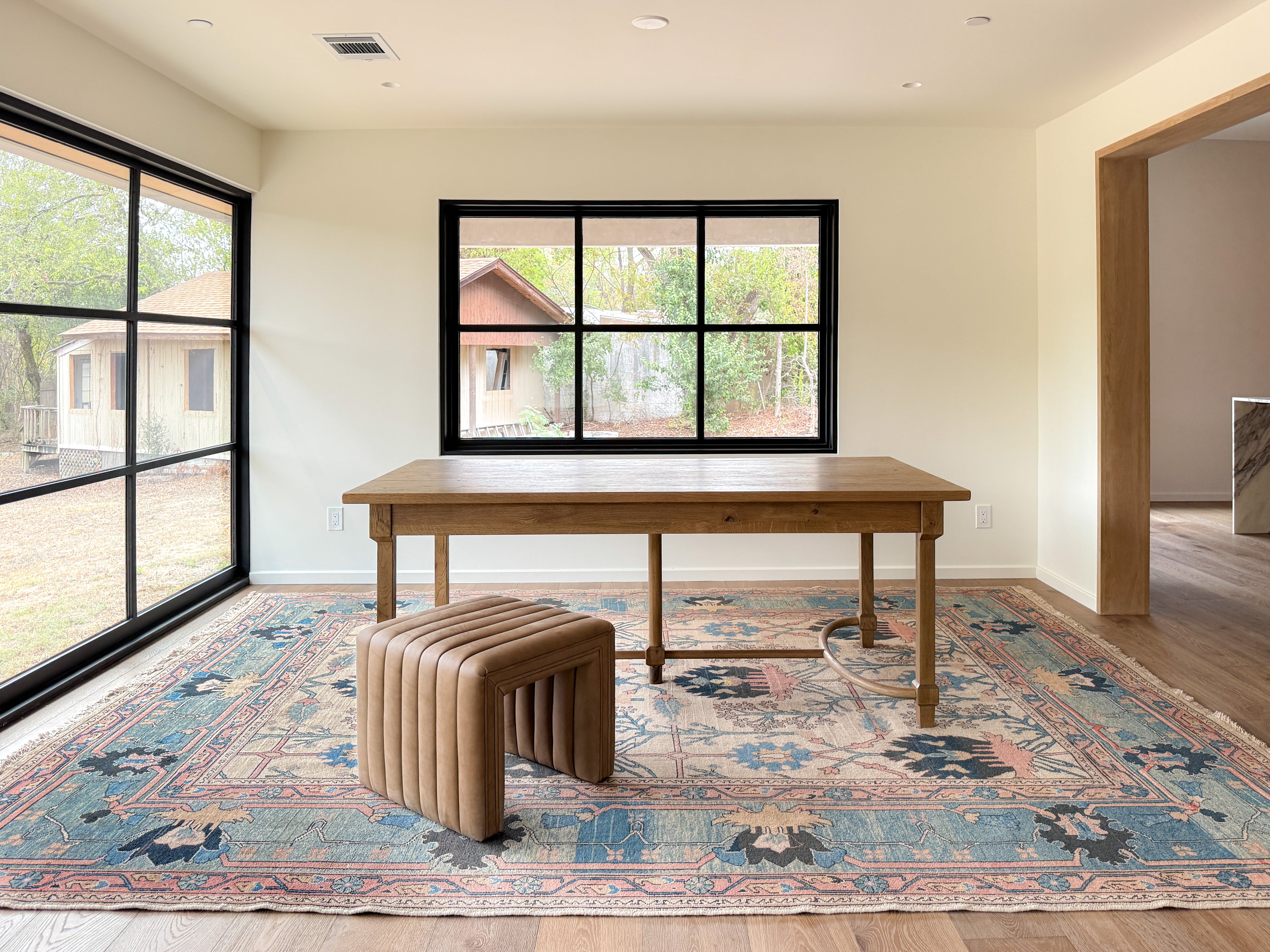 A large blue and beige vintage area rug from a Wooden Looms project in Austin, shown anchoring a wooden table in a modern  dining room.